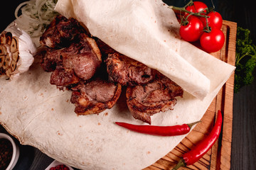 Appetizing fried meat lies on a wooden tray, among the seasonings. Studio photography of food in the cooking industry, dark background