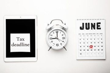 Calendar with tablet computer, alarm clock and text TAX DEADLINE on white background