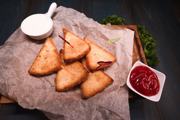 Appetizing fried cheese with sauce on a wooden tray. Studio photography of food in the cooking industry, dark background