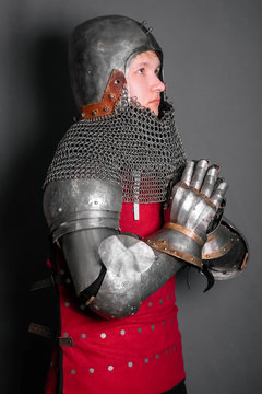 A young knight in medieval armor prays with his hands clasped.