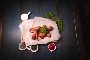 Appetizing fried chicken wings on a wooden tray. Studio photography of food in the cooking industry, dark background