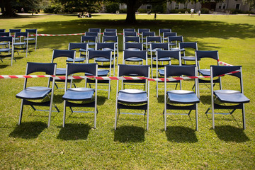 Tens of blue chairs seats lined outside in rows, front view. set on green grass. focal point on...