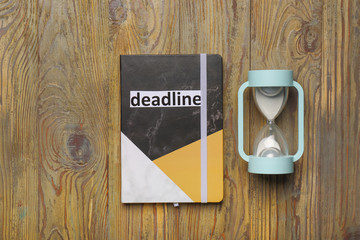 Hourglass with notebook and text DEADLINE on wooden background