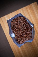 open silver coffee bag, exquisite coffee aroma from the bag, top view, Splash of coffee and milk in white cup isolated on black background movement action, arabica, healthy, fluid, aroma, aromatic, be