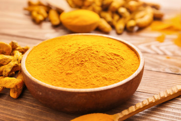 Bowl with aromatic turmeric on wooden background