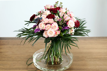 A colorful thriving bouquet of flowers from spray roses and red carnations stands in a vase on the table. soft focus