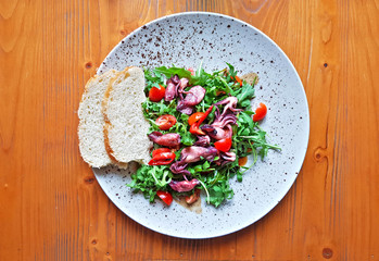 Calamari salad with cherry tomatoes and arugula on wooden table. Top view food.