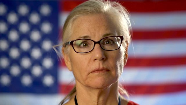 Portrait of a nurse walking from US flag to foreground and showing an extreme sadness and disapproval.