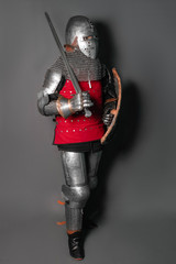 A medieval knight in armor with a shield and a sword in his hands stands in a fighting position and...