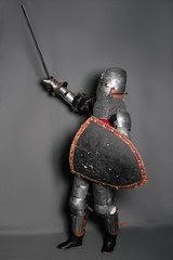 Fototapeta premium A medieval knight in armor with a shield and a sword in his hands stands in a fighting position and waves his weapon.