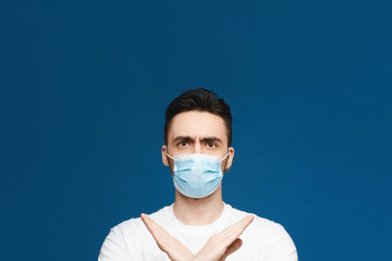 Handsome young man in protective mask against infectious diseases and flu showing gesture enough, isolated at blue background with. Healthcare and health protection concept