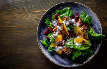 vegetarian salad with beets, spinach, orange, tofu in plate on wooden table background