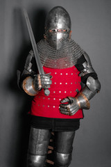 A young knight in medieval armor, armed with a sword, standing on a gray background.