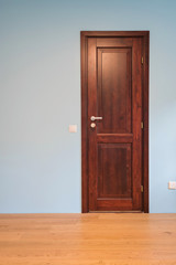 Frontal view to the wooden door in home interior room with wooden floors and blue walls.
