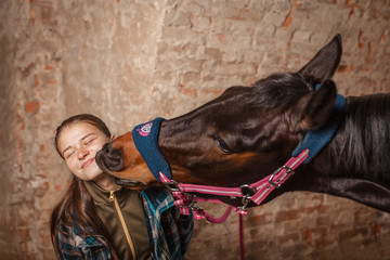  Love for the horse. The bay mare kisses her mistress. A young girl in a checkered trowel loves her...
