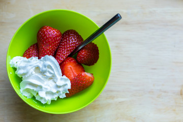 Fresh strawberries and cream in a bowl on a wooden board