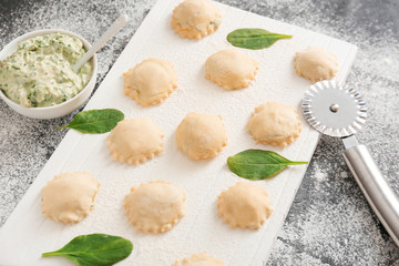 Raw ravioli with spinach and cutter on table