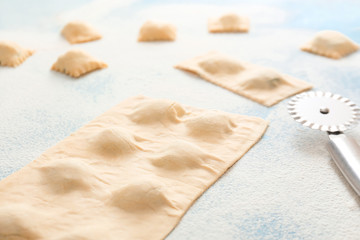 Raw ravioli with cutter on color background