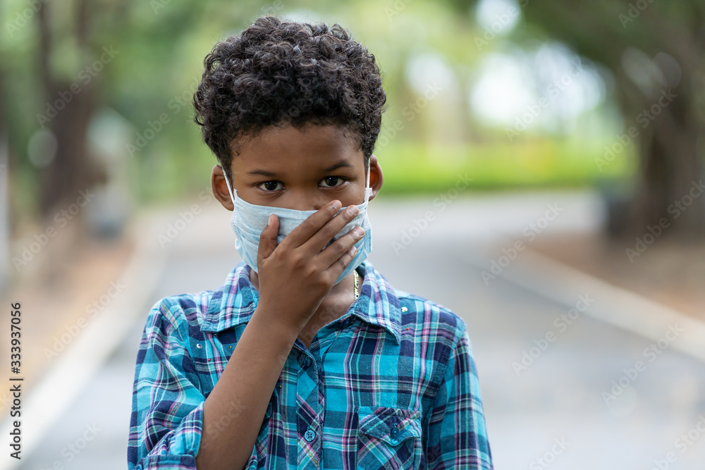 Wall mural Boy put on a protective medical mask for protect PM 2.5 or Coronavirus while standing outdoor and right hand closed his mouth. Boy protect spreading of disease virus with wearing mask.