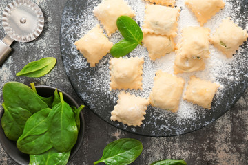 Raw ravioli with spinach and cutter on dark background