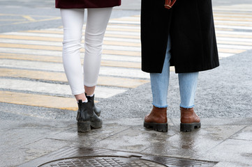 Legs of two girls close up near the pedestrian crossing waiting. Background