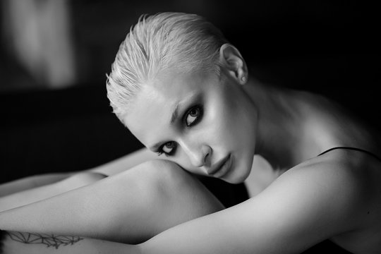 Sadness, depression and loneliness concept. Portrait of sad blonde girl with a short stylish haircut sitting alone on a dark background.