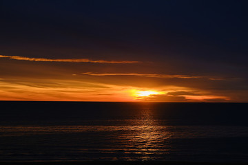 Bright sun on the horizon over the water during sunrise. The reflection of the sun on the sea surface with ripples. Selective focus