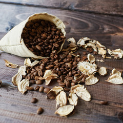 A bag of scattered roasted coffee beans on a brown wooden background