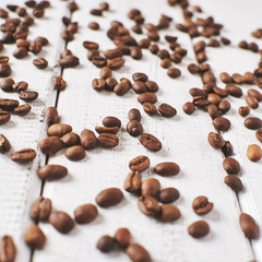 Roasted coffee beans are scattered on the white wooden surface