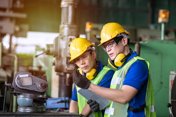 Industrial engineer worker in yellow hard hats dicuss abount production machinery while using laptop in the factory