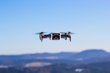 Fototapeta na wymiar Quadcopter drone in flight at blue sky and mountains background