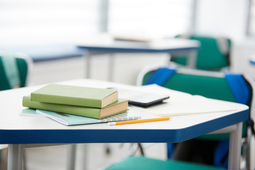 Background close up of green books stacked on desk in school classroom interior, copy space