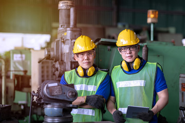 Portrait of industrial engineer worker in yellow hard hats standing near manufacture machinery in the factory