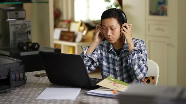 Happy young asian man smiling while studying on laptop at home. online class and home study concept.
