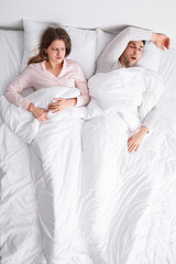 Young irritated woman in bed with snoring husband at home