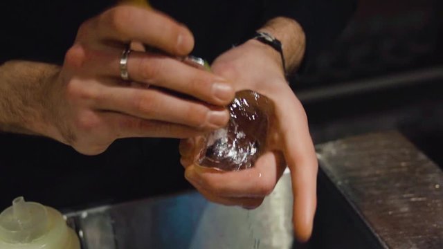 Bartender carves ice cube using ice pick for a cocktail - close up. Barman taillant un gla&ccedil;on pour un cocktail en gros plan.