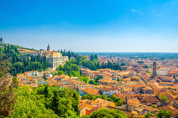 Fototapeta na wymiar Aerial view of Verona historical city centre Veronetta, medieval buildings with red tiled roofs, cypress trees, blue sky background, Veneto Region, Italy. Verona cityscape, panoramic view.