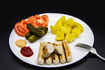 Delicious homemade chicken sausages with tomatoes, cucumbers, potato and souces. Fragrant sausages made from non-GMO chicken. Toasted Mini Sausages from chicken on the plate. Ukrainian tasty food.