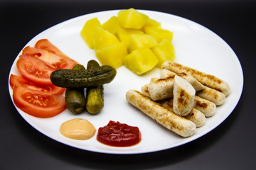 Delicious homemade chicken sausages with tomatoes, cucumbers, potato and souces. Fragrant sausages made from non-GMO chicken. Toasted Mini Sausages from chicken on the plate. Ukrainian tasty food.