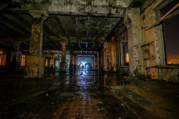 Fototapeta na wymiar Interior of an old abandoned soviet building with cracked ragged walls and leaking roof and wet floor at night with flashlights of stalkers