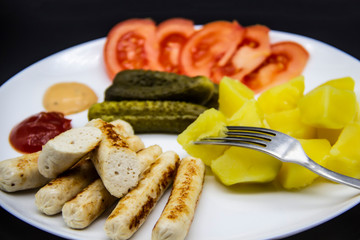 Delicious homemade chicken sausages with tomatoes, cucumbers, potato and souces. Fragrant sausages made from non-GMO chicken. Toasted Mini Sausages from chicken on the plate. Ukrainian tasty food.