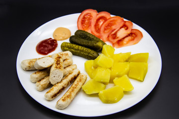 Delicious homemade chicken sausages with tomatoes, cucumbers, potato and souces. Fragrant sausages made from non-GMO chicken. Toasted Mini Sausages from chicken on the plate. Ukrainian tasty food.