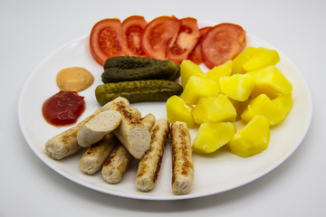 Delicious homemade chicken sausages with tomatoes, cucumbers, potato and souces. Fragrant sausages made from non-GMO chicken. Toasted Mini Sausages from chicken on the plate. Ukrainian tasty food.