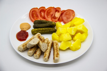 Delicious homemade chicken sausages with tomatoes, cucumbers, potato and souces. Fragrant sausages made from non-GMO chicken. Toasted Mini Sausages from chicken on the plate. Ukrainian tasty food.