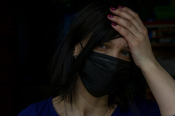 A girl in a medical mask holds her head in despair