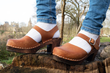 A beutiful pair of wooden clog shoes worn by a woman standing on a log