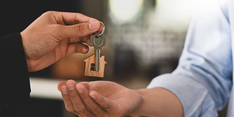 Cropped image Hands of real estate agent offering/giving a house key to smart man in blue shirt...