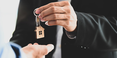Cropped image Hands of real estate agent offering/giving a house key to smart man in blue shirt while standing together over modern bank as background. Broker/Seller/Dealer concept.