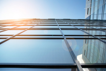 Obraz premium Facade of modern glass building at sunset. Warm and cool tone contrast. Sun flare.