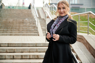 Photo of a fashionable blonde girl in a coat on the stairs outdoors in the spring city